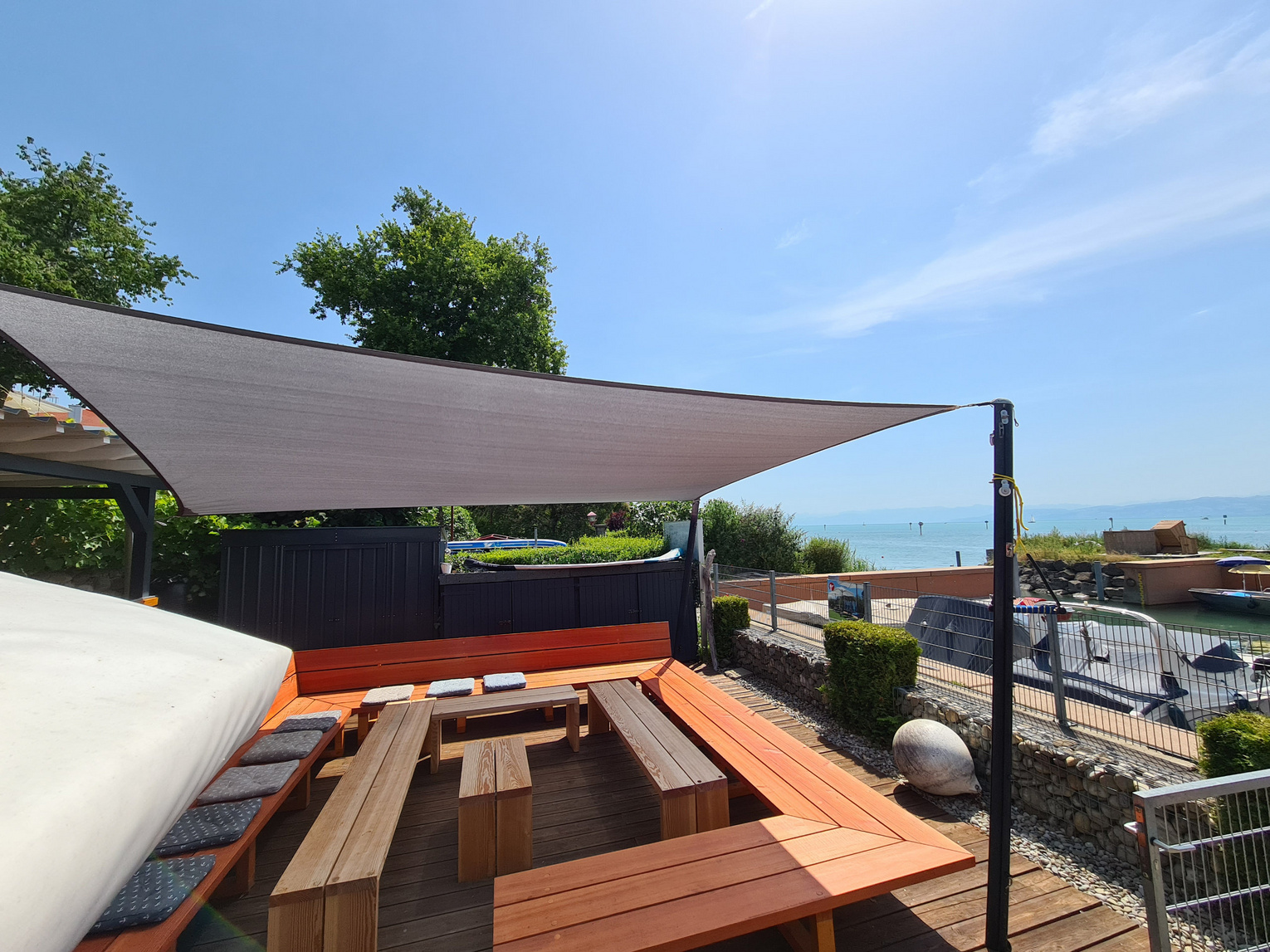 Moderne Holzterrasse mit Sonnensegel und Blick aufs Wasser
