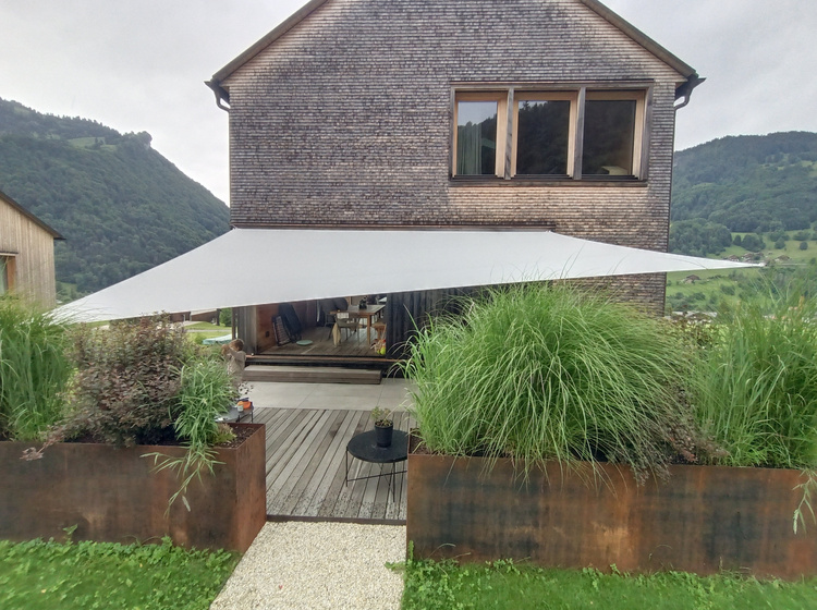 Kleines Haus vor Bergpanorama mit Sonnensegel